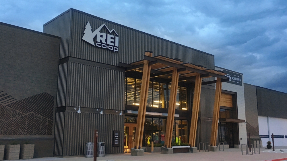 An REI storefront in Fort Worth, Texas shot against a cloudy sky.